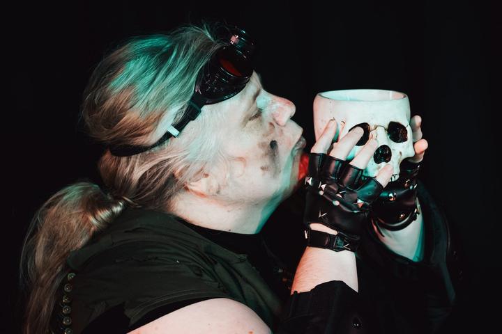 A performer with goggles on their forehead holds a white skull close to their face