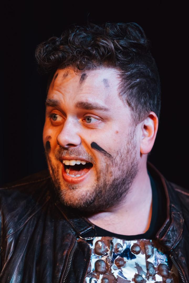 A performer in a leather jacket laughs with delight, face streaked with black paint