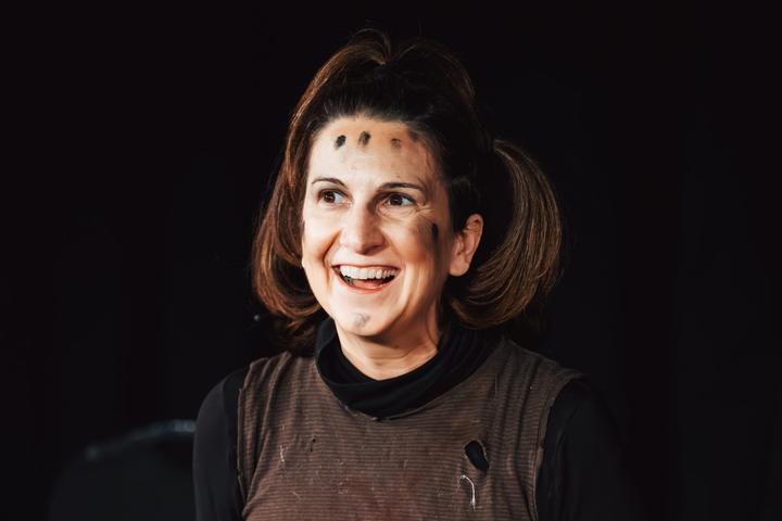 A performer with hair in pigtails and black face paint laughs on stage