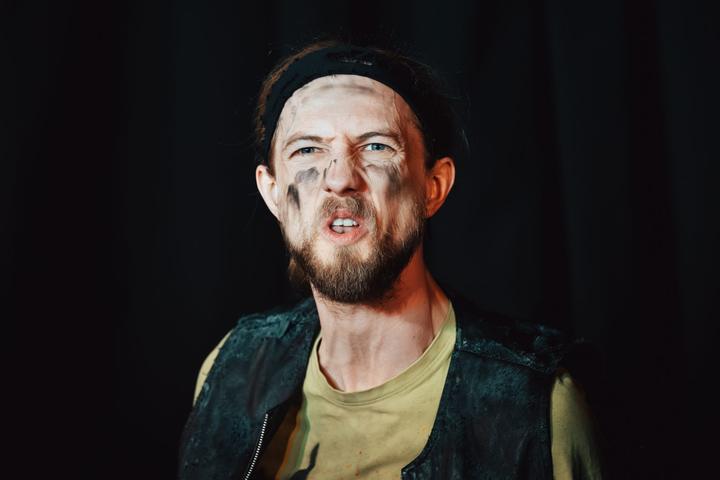 A bearded performer with a headband snarls toward the camera