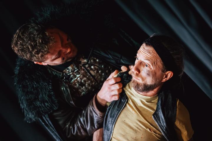 Two performers face each other at close range in dramatic stage lighting