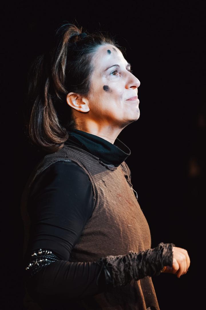 A performer with dark face paint looks upward into a spotlight
